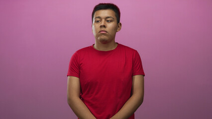 Man standing with face visible and clasped hands in pink studio wearing red t shirt and direct gaze; serious introspection calm.