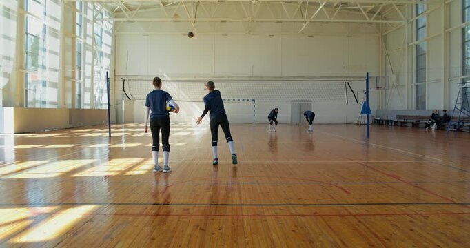 Girls practicing overhand serving technique. Female volleyball players take turns practicing serving the ball over the net.