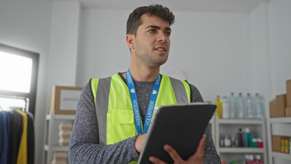 Man holds tablet for checking warehouse items as hispanic volunteer tracks donations inventory in aid role as dedicated guy.