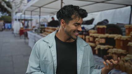 Man makes air guitar gesture with hands in a bustling outdoor street market by rows of pottery stalls; playfulness.