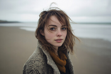 Young woman in warm clothes on beach with gray sky
