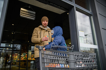 Father and son spending time together during a winter grocery trip, walking with a shopping cart, sharing snacks, and enjoying everyday family moments outdoors near a store.