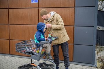 Father and son spending time together during a winter grocery trip, walking with a shopping cart, sharing snacks, and enjoying everyday family moments outdoors near a store.