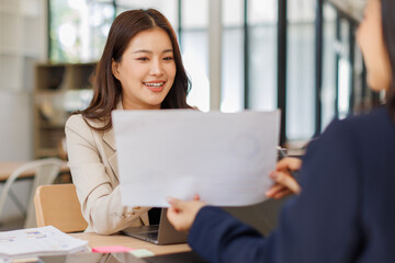 Asian business team colleagues analyzing financial charts and data on computer screen in a bright...