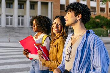 Diverse group of college students standing outdoors on university campus, holding books and folders, smiling, and looking forward to the future
