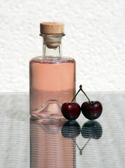 Minimalist still life with ripe cherries and homemade compote in a small vintage bottle on a glass-topped table.