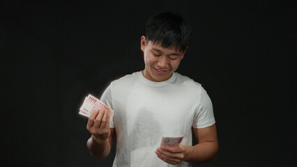 Young man counting taiwanese dollar banknotes over isolated black background with a smile