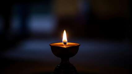 Small diya lamp flame burning in traditional metal bowl on dark blue bokeh background for festival
