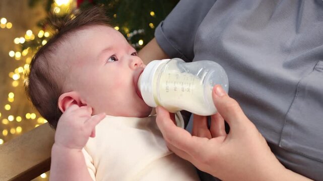 Close-up of a baby being held on an adult's lap and lovingly fed with breast milk from a bottle.