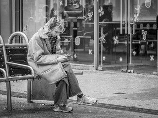 Person sitting alone on a bench while using a smartphone, reflecting digital dependency and modern isolation
