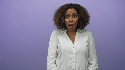 Woman with mouth open and wide eyes in lavender studio wearing a white shirt and relaxed posture;...