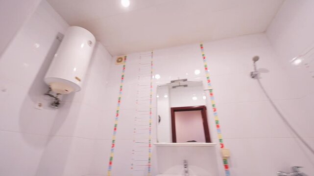 compact bathroom with white tiles, pedestal sink, toilet, bathtub with showerhead, colorful tile border, mirror above sink, minimalistic design, clean lines.
