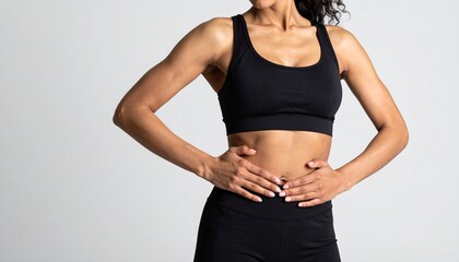 Fit woman in black sportswear poses with hands on her stomach, fitness concept.