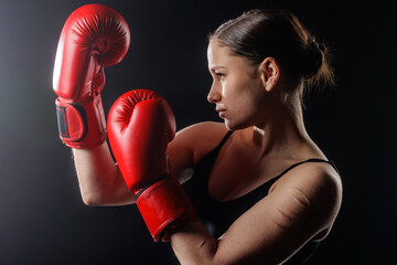 Female boxer in red gloves, side view pose in dark studio with copy space