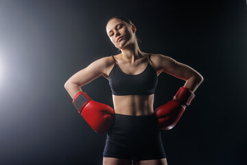 Confident female boxer in red gloves posing in dark studio with copy space