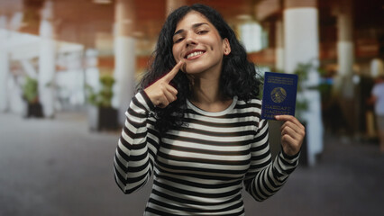 Young brunette woman holding belarus passport pointing finger to passport in airport terminal with...