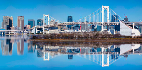 Rainbow Bridge by Daiba Park and Odaiba Seaside Park in Minato City, Tokyo, Japan, a calm waterfront scene blending architecture and coastal beauty with water reflections