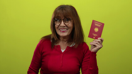 Senior hispanic woman smiling while holding a german passport against a vibrant yellow background, exemplifying travel and identification themes. © Krakenimages.com
