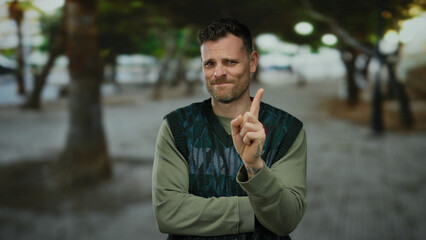 Young man gesturing no with his finger in an urban street, showcasing a confident expression amid a blurred city background, highlighting his casual style and expressive demeanor.