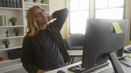 Man sitting at desk typing at computer holds neck in building with slouched posture; discomfort...