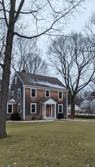 Snow melting on a large brick house with trees and green grass