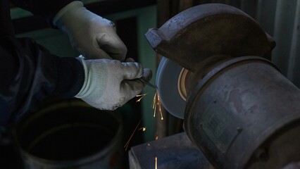 Industrial worker grinding metal rod with bench grinder in factory
