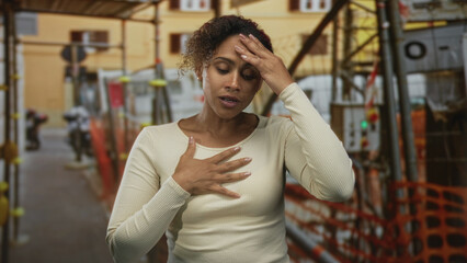 Woman clutching chest with hand and touching forehead in building under construction; anxiety safety.
