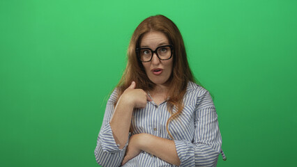 Fototapeta premium Caucasian woman wearing long sleeve striped shirt points thumb to chest in green studio; confidence self belief trust.