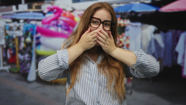 Woman covers mouth with hands amid colorful souvenir stall on a bustling urban street market scene; surprise.