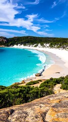 Fototapeta premium Coastal view of turquoise water, white sand beach, and lush green vegetation under a bright blue, partly cloudy sky