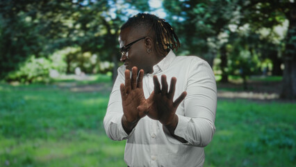 Man raising hands palms out in forest, white shirt and glasses, turned aside with defensive hand gesture; unease refusal.