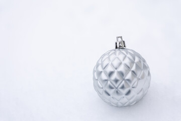 Silver Christmas ball ornament with geometric texture placed on snow, clean white background with copy space, minimal and elegant winter holiday decoration suitable for seasonal design and advertising