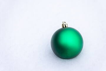 Green Christmas ball ornament placed on snow with clean white background and copy space, minimal winter and holiday decoration concept suitable for seasonal design and advertising.
