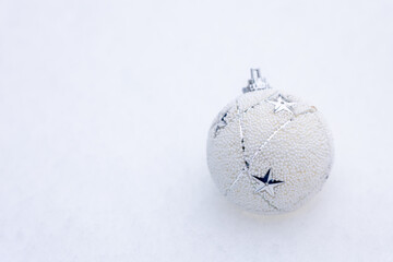 White Christmas ball ornament with star details resting on snow, clean white background with copy space, elegant winter holiday decoration suitable for seasonal design, branding, and advertising.