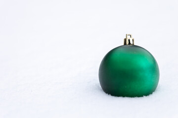 Green Christmas ball ornament placed on snow with clean white background and copy space, minimal winter and holiday decoration concept suitable for seasonal design and advertising.