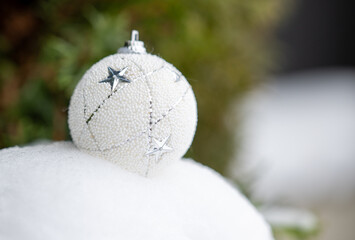 White Christmas ball ornament with silver star details resting on fresh snow, soft natural background, elegant winter holiday decoration suitable for seasonal design, branding, and advertising.