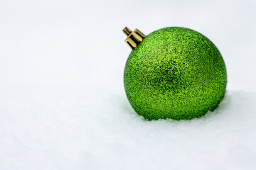 Green glitter Christmas ball ornament resting on fresh snow with white background and copy space, elegant and calm winter holiday decoration suitable for seasonal design, marketing, and advertising.