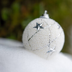 White Christmas ball ornament with silver star details resting on fresh snow, soft natural background, elegant winter holiday decoration suitable for seasonal design, branding, and advertising.