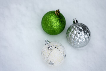 Three Christmas ball ornaments in green, silver, and white arranged on fresh snow with clean background and copy space. Minimal winter holiday composition suitable for Christmas design, advertising, a