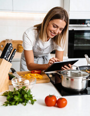 Smiling young woman using digital tablet while cooking in kitchen at home