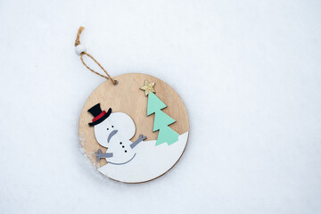 Wooden ornament with snowman and tree lying on snow. Minimal winter scene with copy space, suitable for greeting cards, decorations, winter design and seasonal backgrounds.