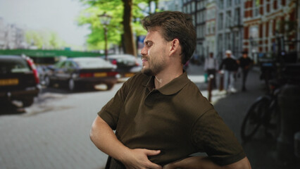 Man clutching right side and holding lower back on city street with backache near parked cars and...