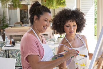 Obraz premium Asian mother with her daughter painting at easel in backyard patio in splattered aprons