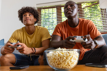 Male friends playing games with controllers in living room with popcorn bowl on coffee table © wavebreak3
