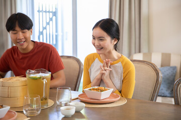 Asian couple sitting at dining table at home with noodle salad, steamer and iced tea