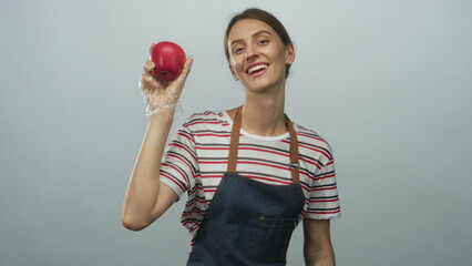 Woman wearing striped shirt, apron and glove holding a red apple aloft in pale blue studio; healthy...