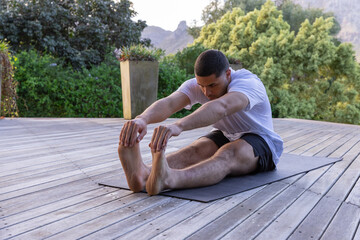 Man stretching on exercise mat on deck with planter wearing white t-shirt and black shorts