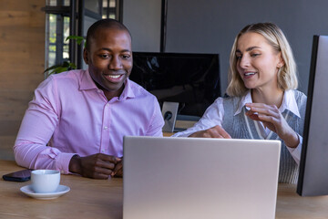 Diverse coworkers discussing data on laptop at office desk with coffee cup