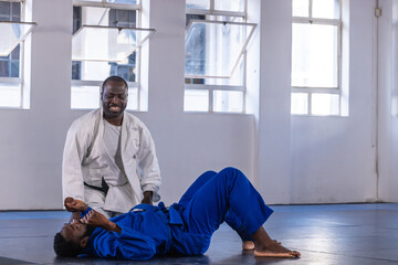 African american instructor guiding student practicing grappling in dojo on mats wearing gis