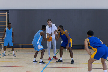 Diverse basketball team following coach's practicing defense at gymnasium with basketball © wavebreak3